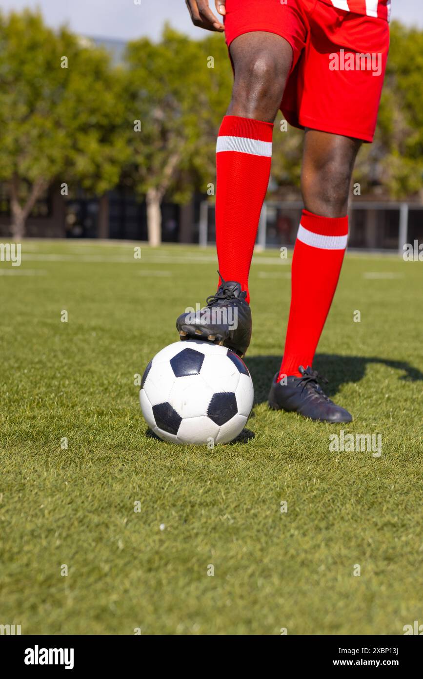 Il giocatore di calcio afroamericano sta in piedi sul campo di calcio con piede su palla Foto Stock