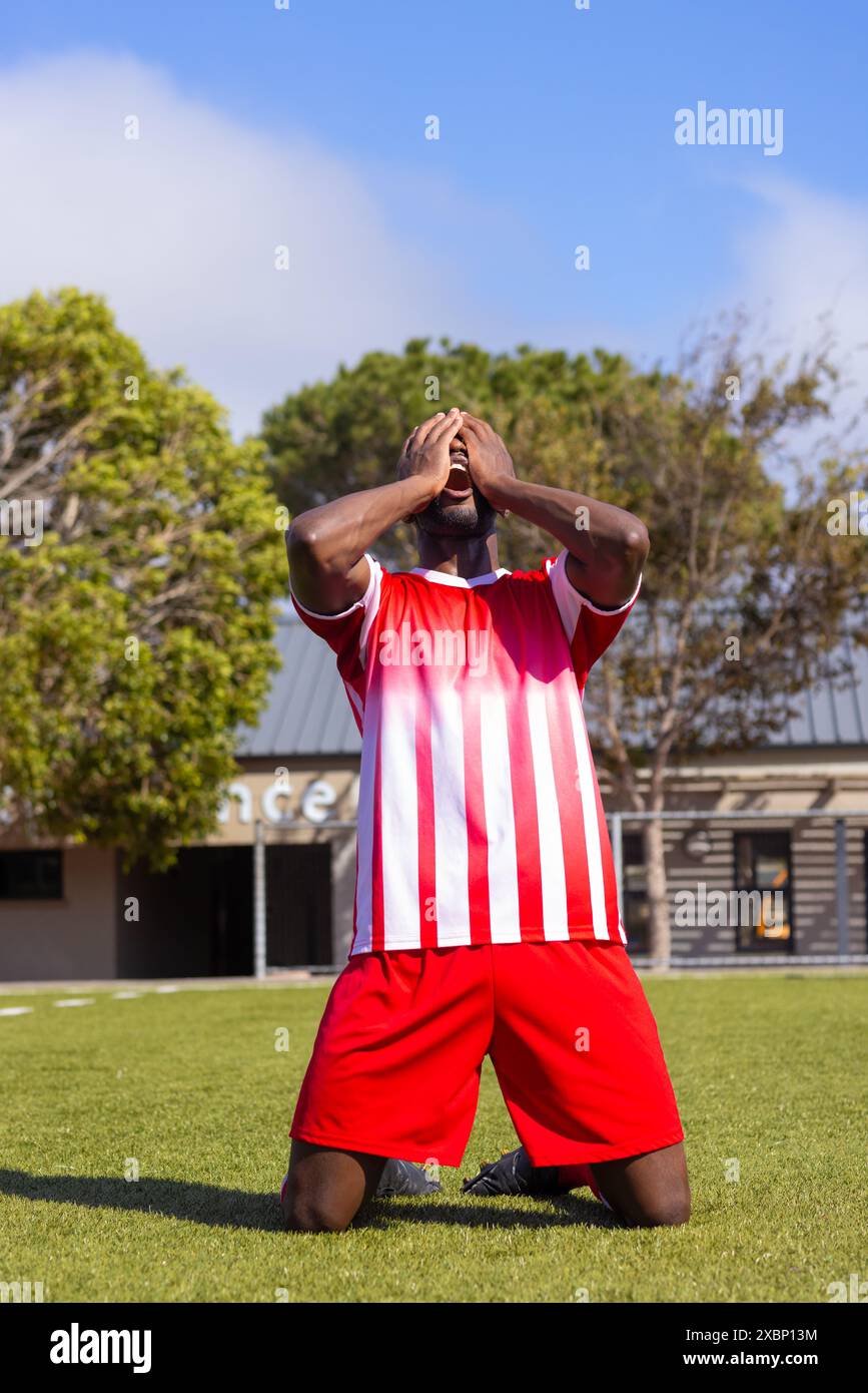 Giocatore di calcio afroamericano inginocchiato sull'erba, apparendo emotivo Foto Stock