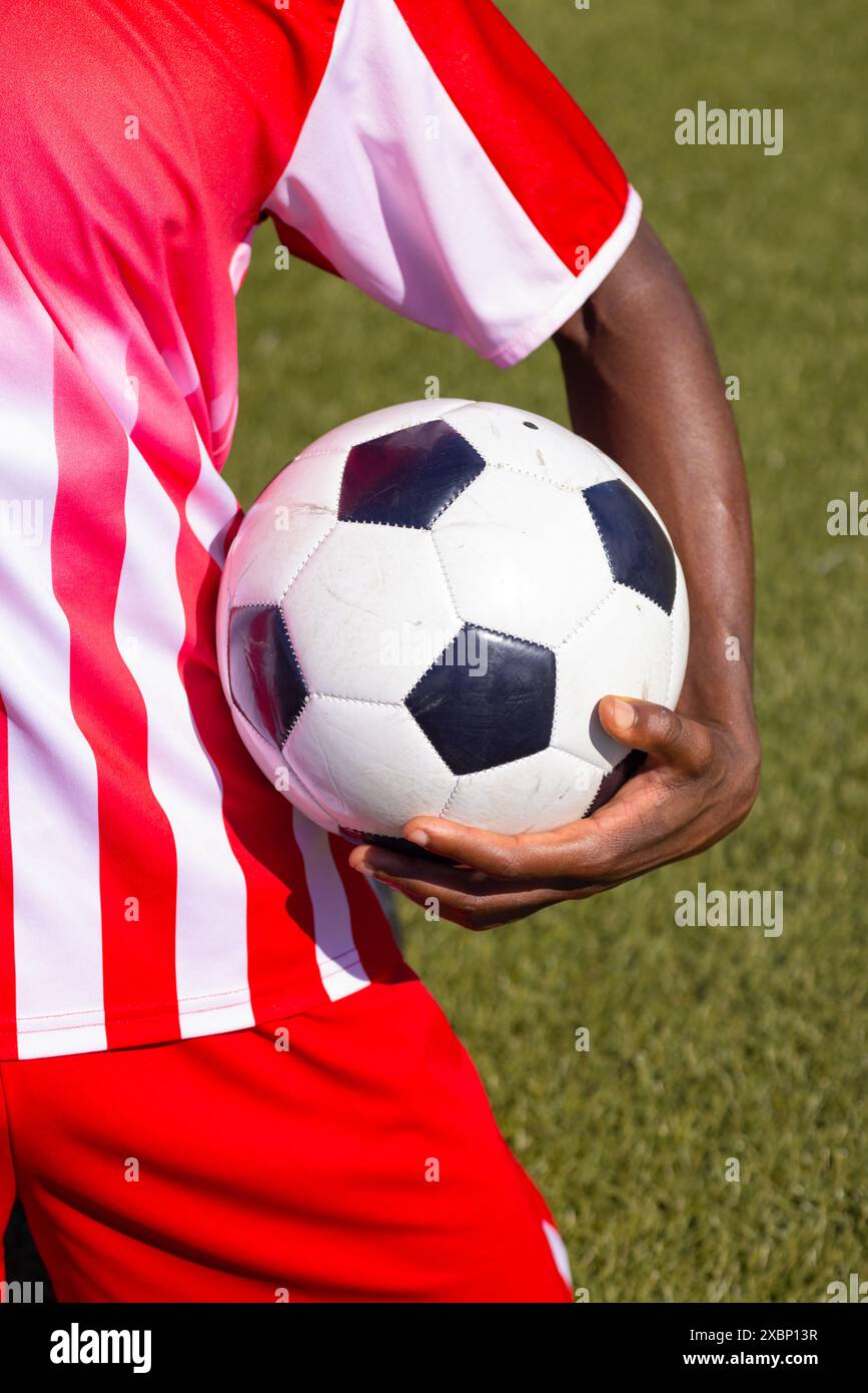 Giocatore di calcio afroamericano con palla da calcio in divisa sportiva rossa e bianca Foto Stock