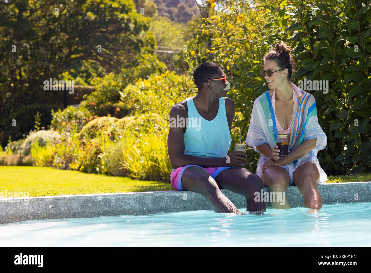 Una coppia variegata si gode un drink in piscina, crogiolandosi al sole estivo e godendo delle vacanze Foto Stock