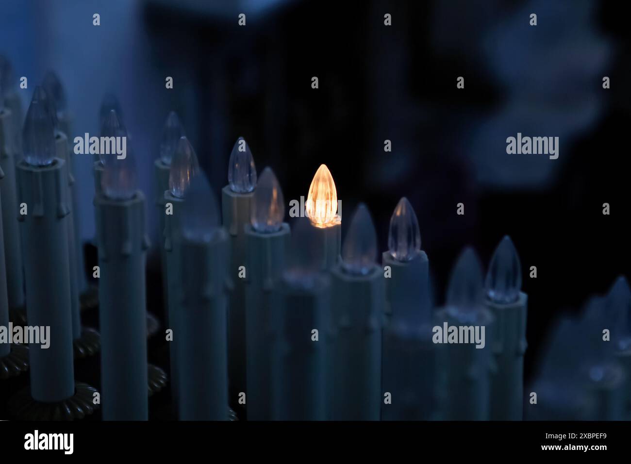 Una candela elettrica accesa che si distingue dalle altre candele spente in una chiesa, creando un concetto di fede, speranza e fede Foto Stock