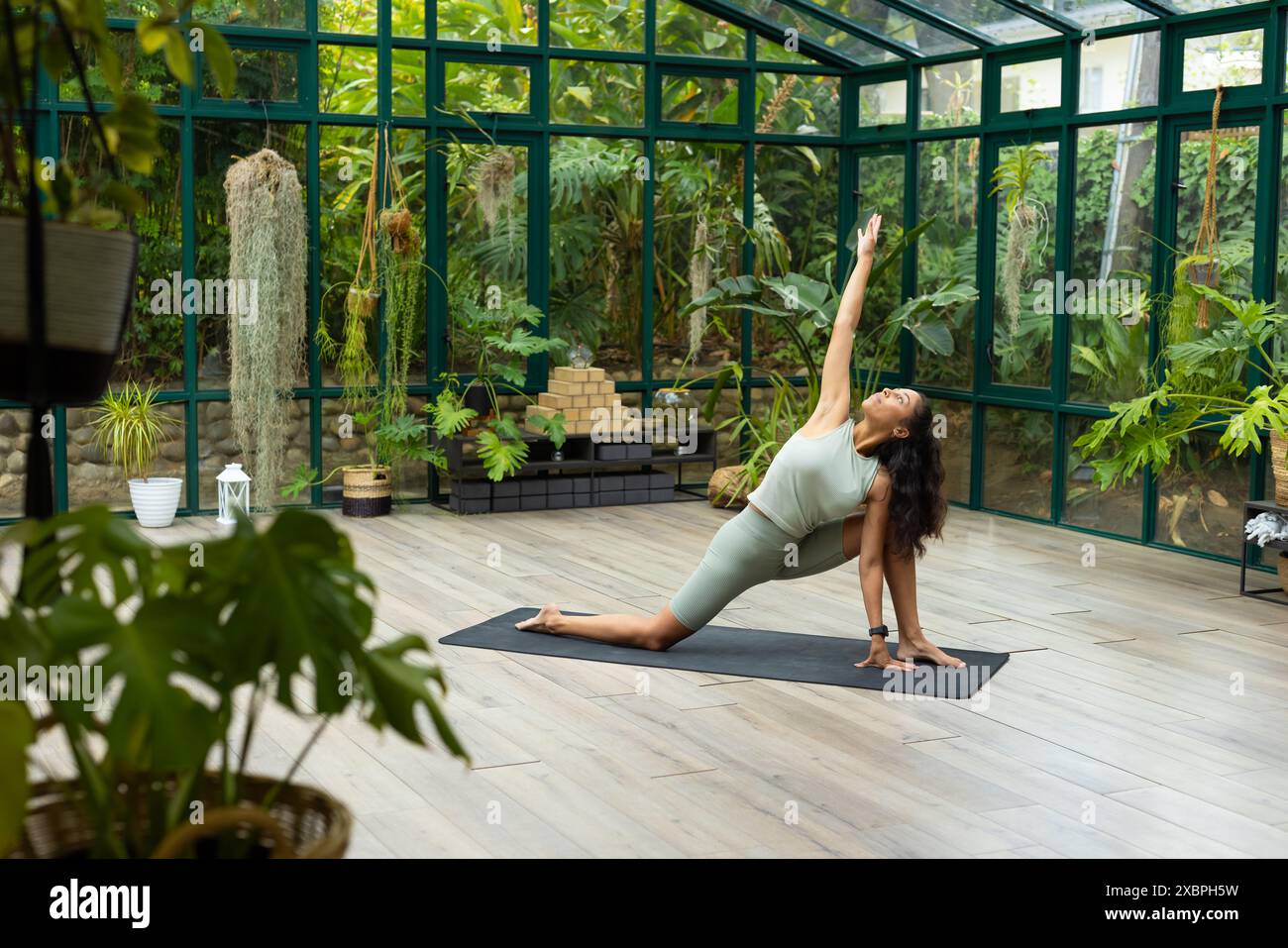 donna birazziale che pratica yoga in una casa di vetro, esegue una posa di affondo basso, copia spazio Foto Stock