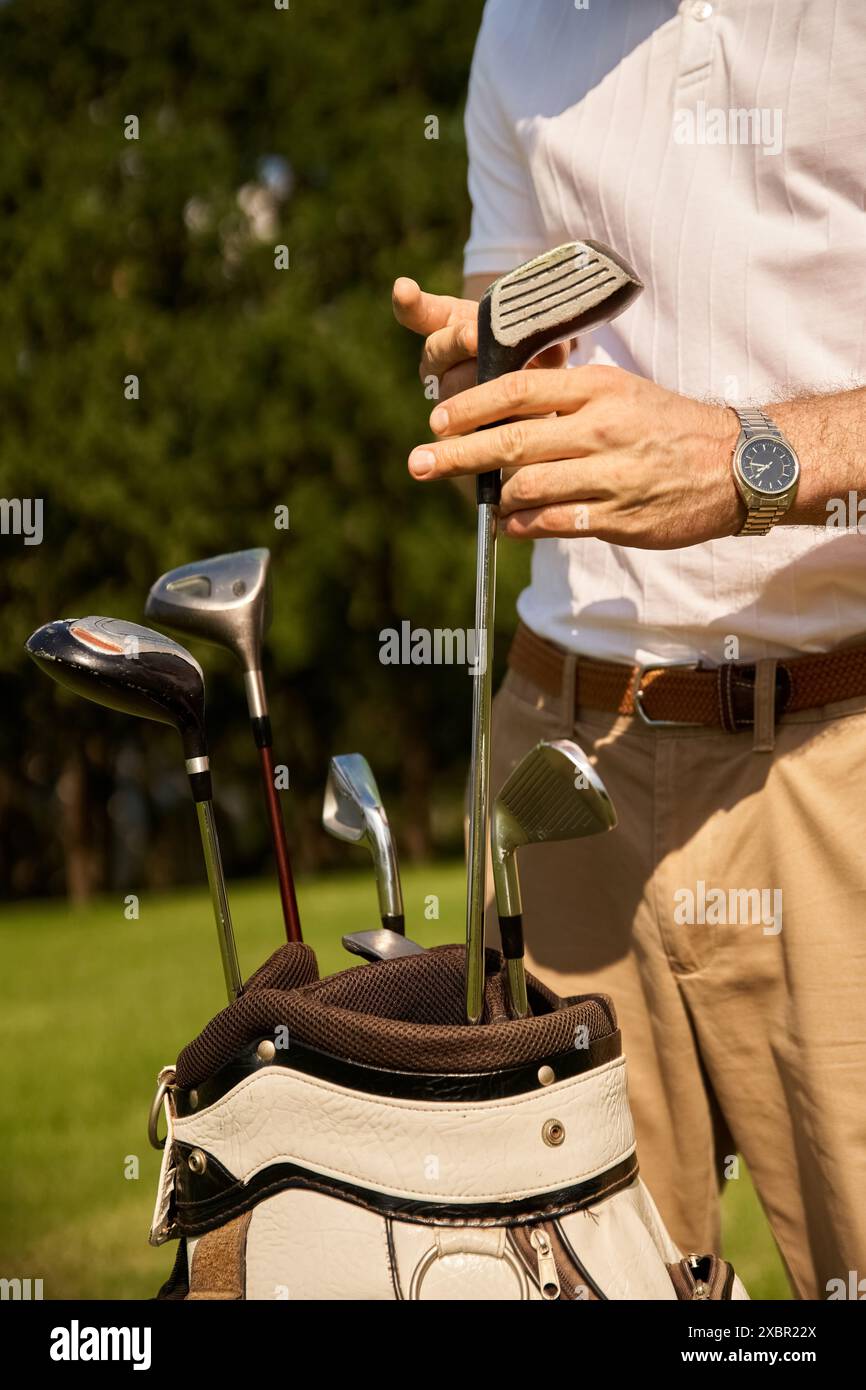 Un giovane uomo alla moda che indossa abiti eleganti e mette le sue mazze da golf in una borsa su un campo verde in un prestigioso golf club. Foto Stock