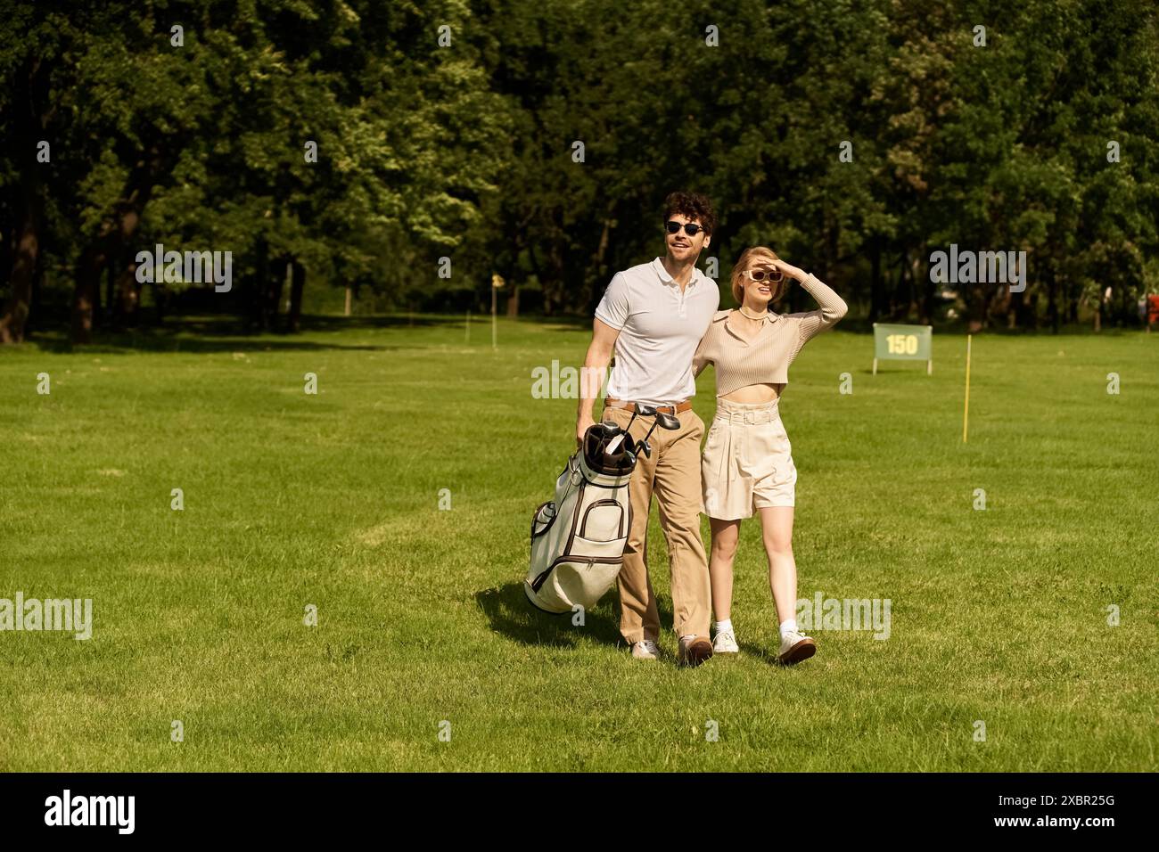 Una giovane coppia elegante fa una piacevole passeggiata su un pittoresco campo da golf, godendosi compagnia. Foto Stock