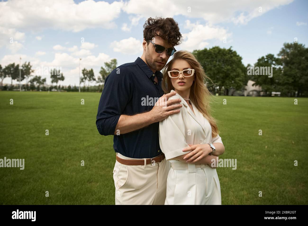 Un uomo e una donna, elegantemente vestiti, si uniscono in un lussureggiante campo verde, incarnando una vita di lusso e raffinatezza. Foto Stock