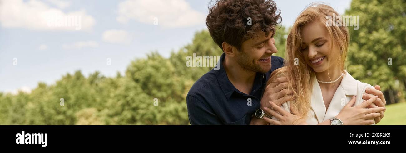 Una giovane coppia elegante, vestita con un abbigliamento elegante, si abbraccia in un lussureggiante campo verde, esprimendo amore e connessione. Foto Stock