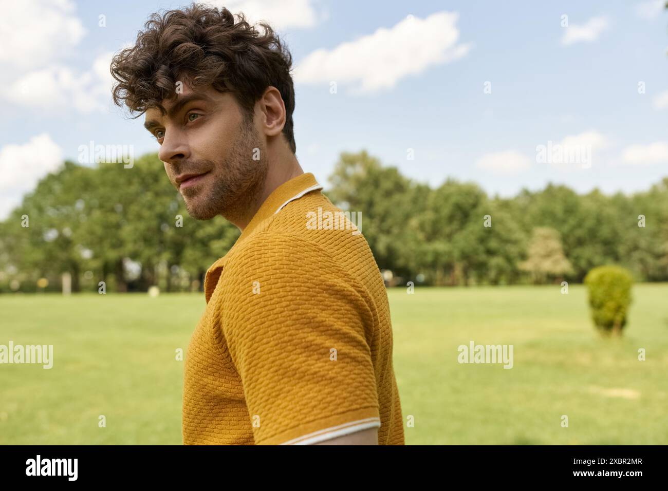 Un uomo con una camicia gialla si trova in un vasto campo verde. Foto Stock