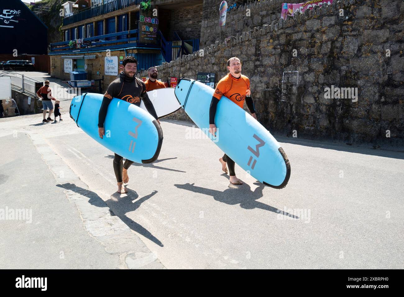 Un istruttore di surf della Cornish Wave Surf School e due studenti che portano le loro tavole da surf dopo una lezione di surf a Towan Beach a Newquay in Foto Stock