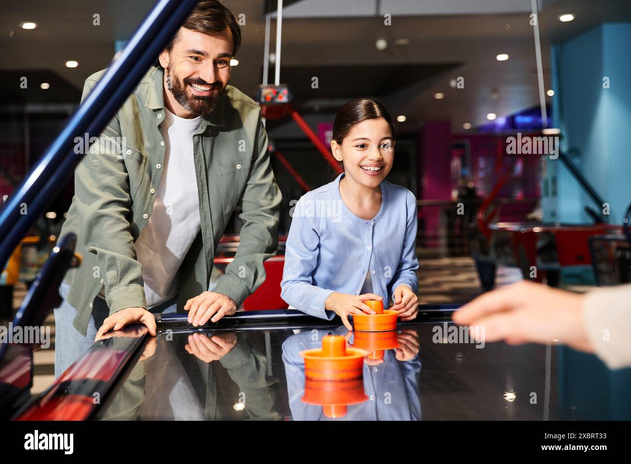 padre e figlia si impegnano in una partita amichevole di hockey da tavolo in una zona di gioco in un centro commerciale, creando un'atmosfera vivace e divertente Foto Stock