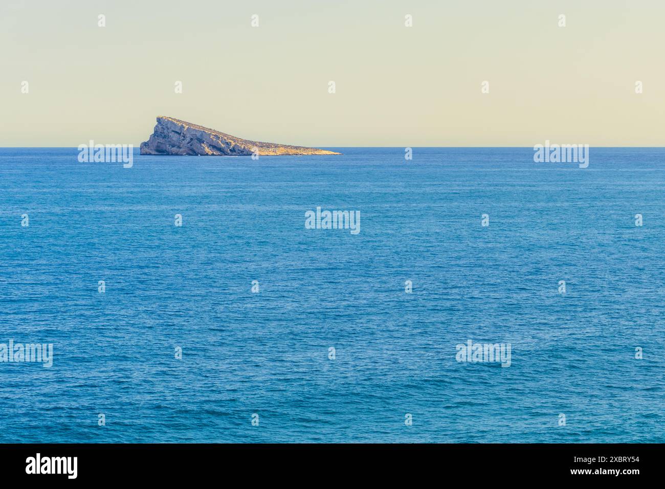 Questa immagine cattura la bellezza tranquilla del Mar Mediterraneo, con il piccolo profilo roccioso dell'Isla de Benidorm. Foto Stock