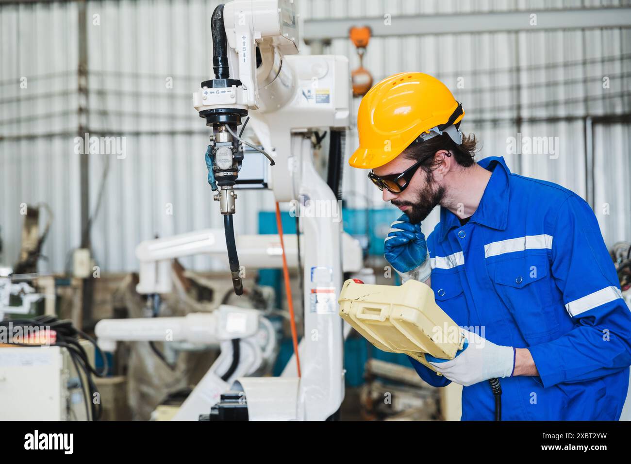 ingegnere che controlla il braccio del robot in fabbrica. controllo del funzionamento del braccio del robot. Tecnologia, automazione, innovazione e concetto ingegneristico. Foto Stock