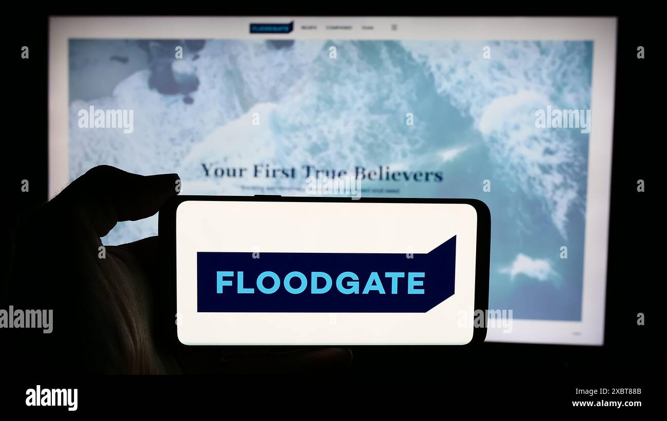 Persona che detiene un cellulare con il logo della società di venture capital statunitense Floodgate Fund LP di fronte alla pagina Web aziendale. Mettere a fuoco il display del telefono. Foto Stock