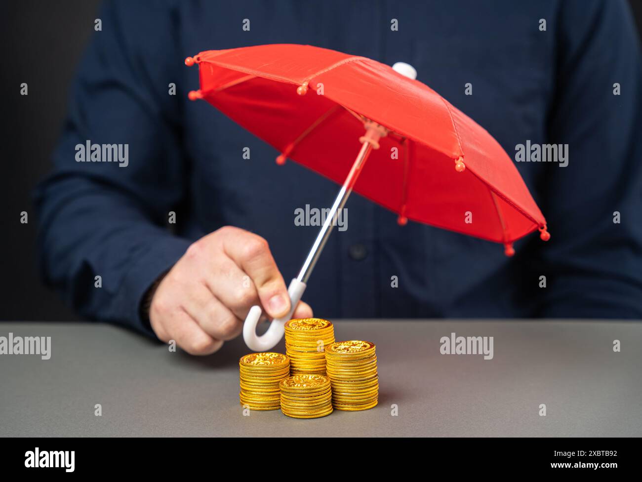Uomo d'affari che tiene l'ombrello sopra una pila di monete. Concetto di assicurazione contro il rischio finanziario. Investimenti, depositi e prestiti. Rischi e transazioni monetarie. Foto Stock