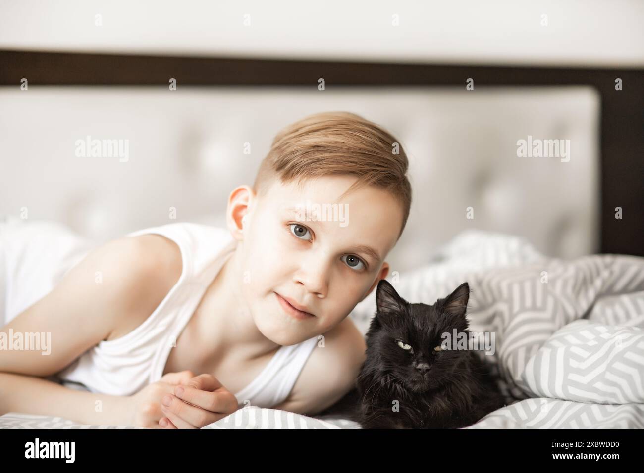 Ragazzo adolescente giace sul letto con il gatto nero del migliore amico. Foto Stock