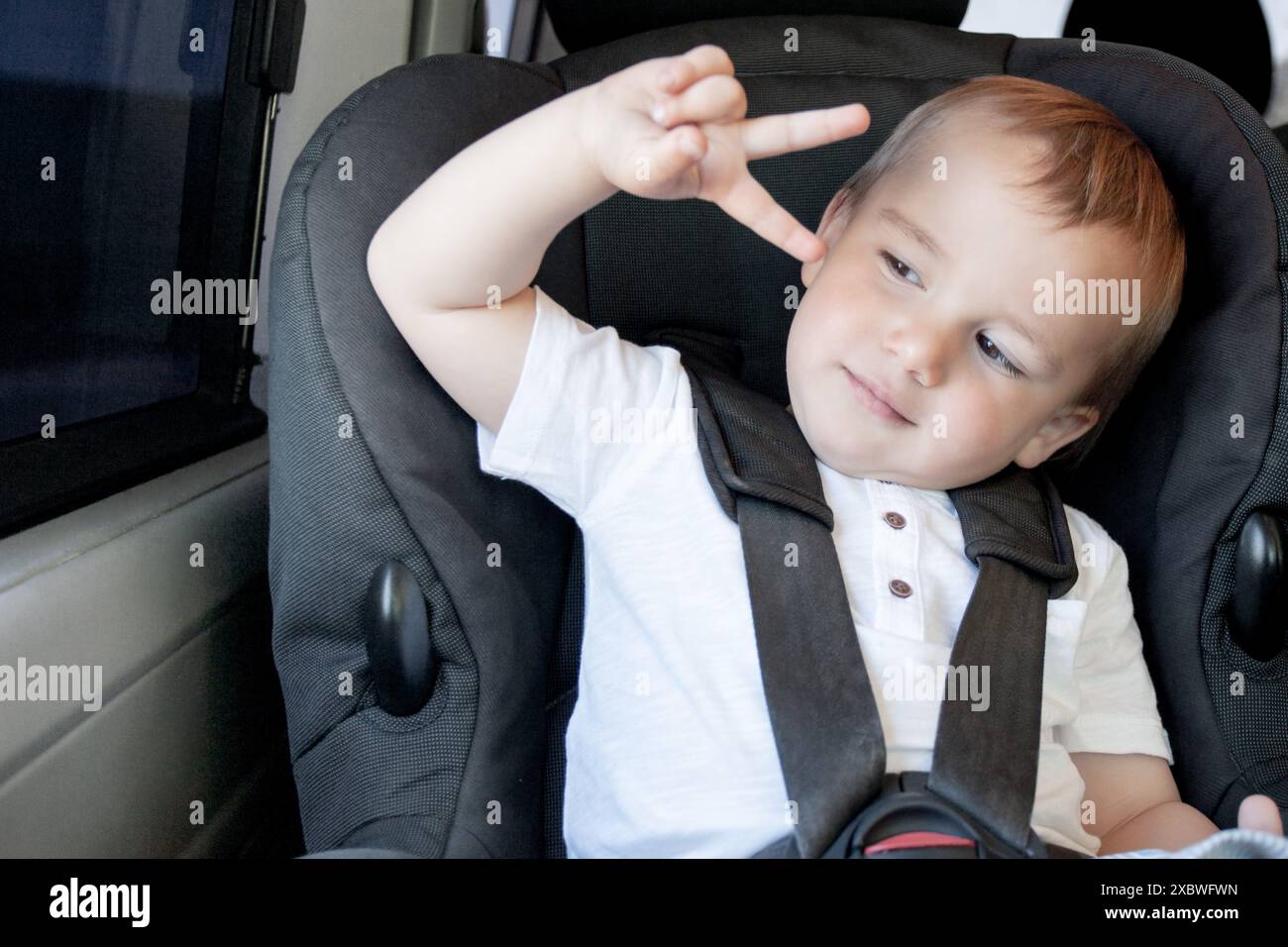 Bambino seduto su un seggiolino in macchina che fa la mano della vittoria. Segno di pace. Foto Stock