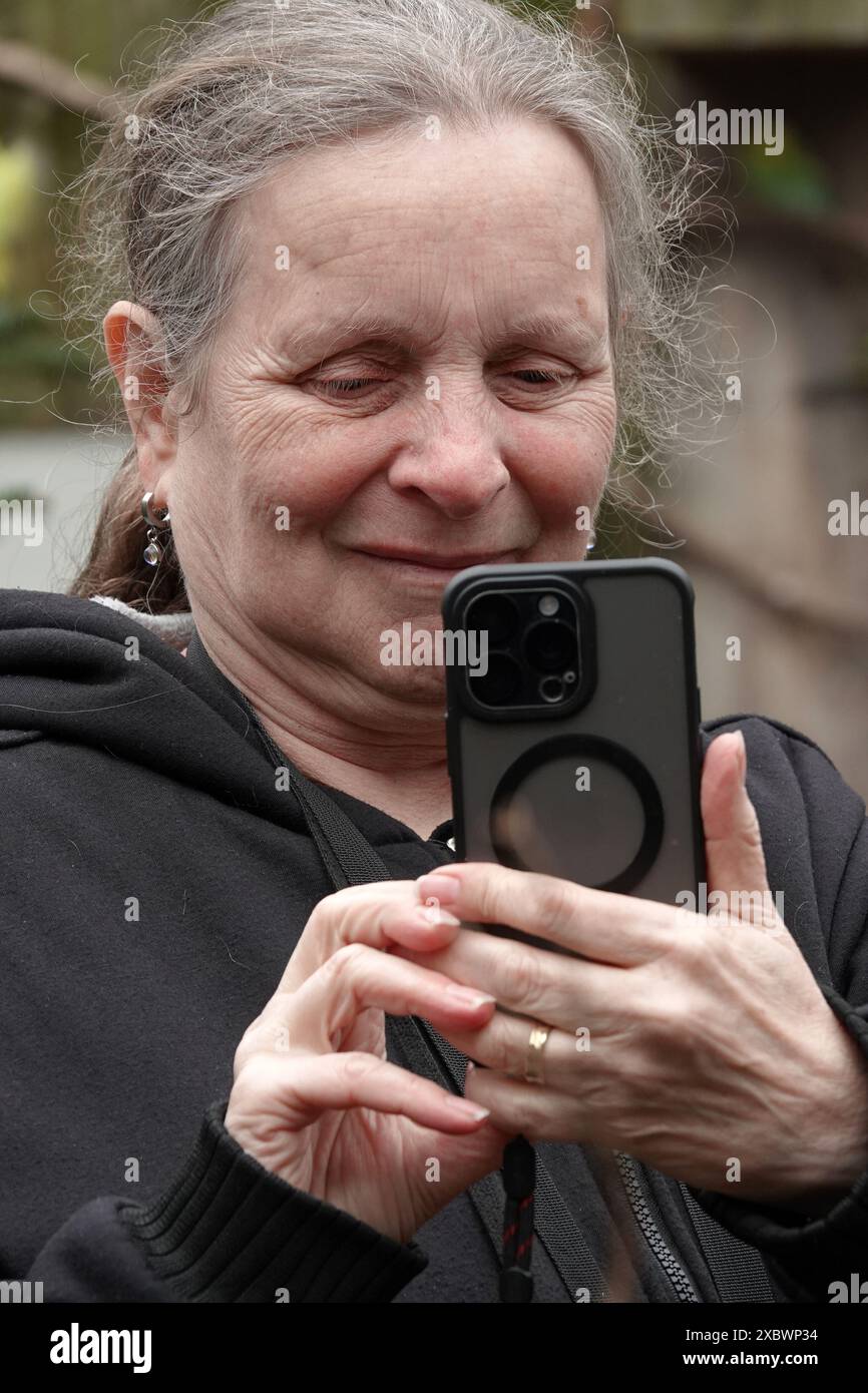 Donna caucasica anziana di 65 anni sta usando il suo smartphone per scattare una foto Foto Stock