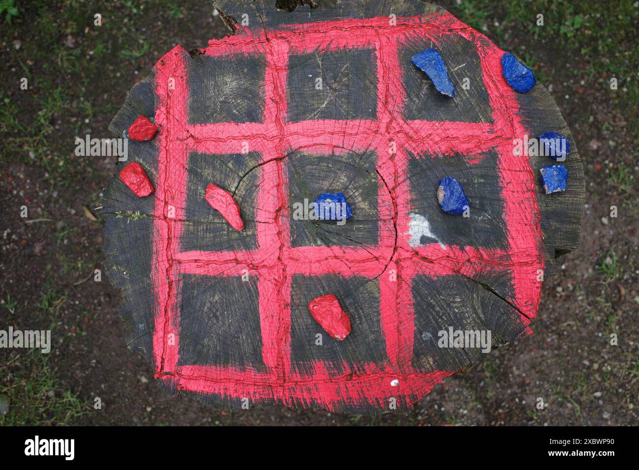 TIC-tac-toe board dipinto su un tronco di albero con pietre colorate per giocare Foto Stock