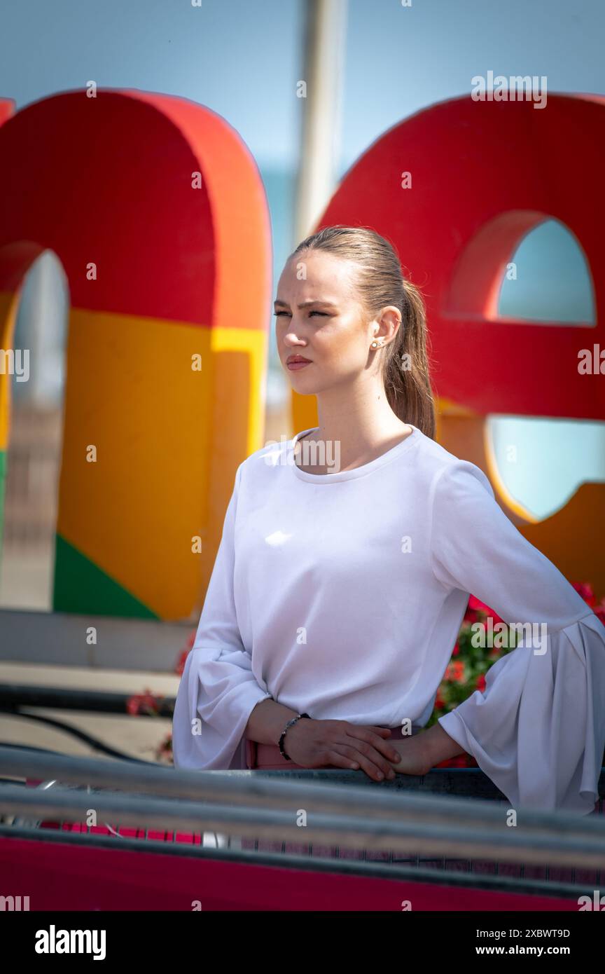 Uno splendido modello biondo si posa graziosamente vicino all'iconico logo della città di Riccione, Italia. Foto Stock