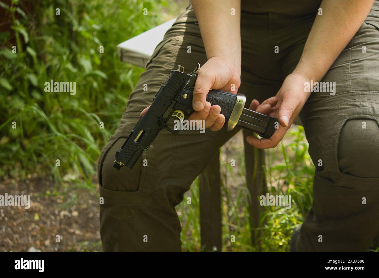 qualcuno con i pantaloni verdi e' seduto con una pistola in mano per strada Foto Stock