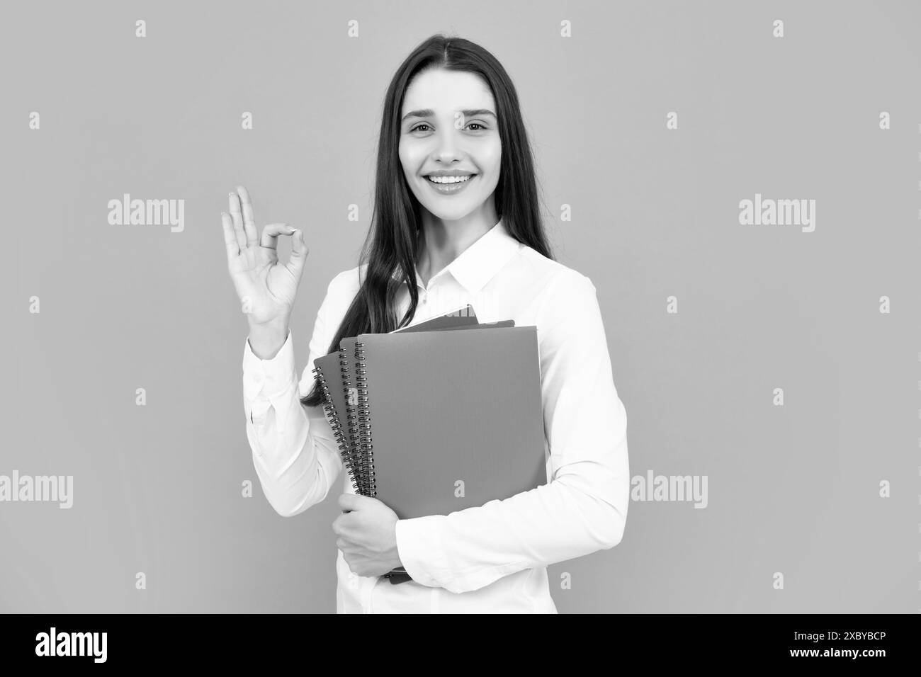 Istruzione degli studenti nel concetto di college universitario di scuola superiore. Felice ragazza giovane che tiene il libro di nota. Studente ragazza dall'aspetto intelligente con segno ok Foto Stock