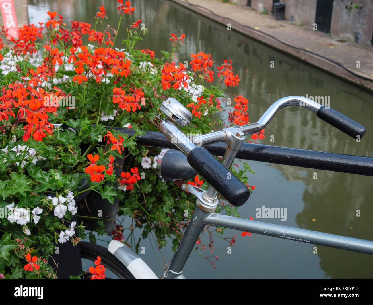 Una bicicletta si appoggia contro una ringhiera, decorata con fiori in fiore, lungo un canale con acqua riflettente, utrecht, Paesi Bassi Foto Stock