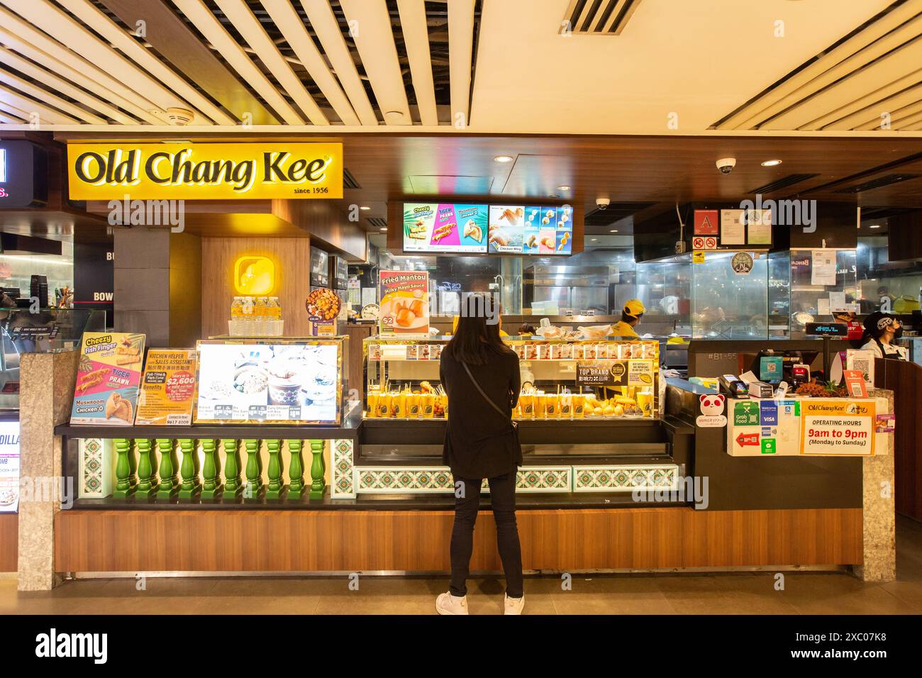 Retrospettiva di una donna che ordina la sfoglia al curry o altri snack finger food presso l'outlet Old Chang Kee. Singapore. Foto Stock