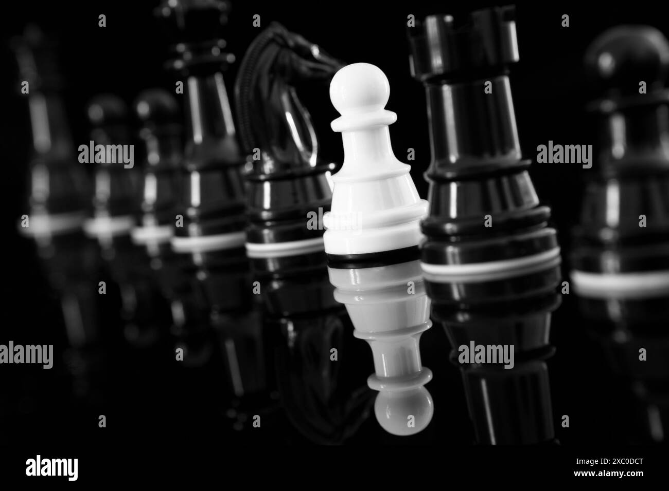 Primo piano di pedone bianco tra pezzi scacchistici neri con riflesso Foto Stock