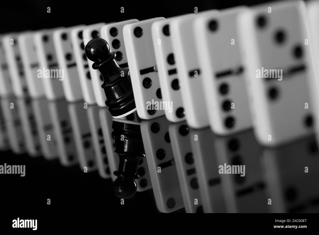 Primo piano di una pedina scacchiera nera tra pezzi di domino. individualità concettuale Foto Stock