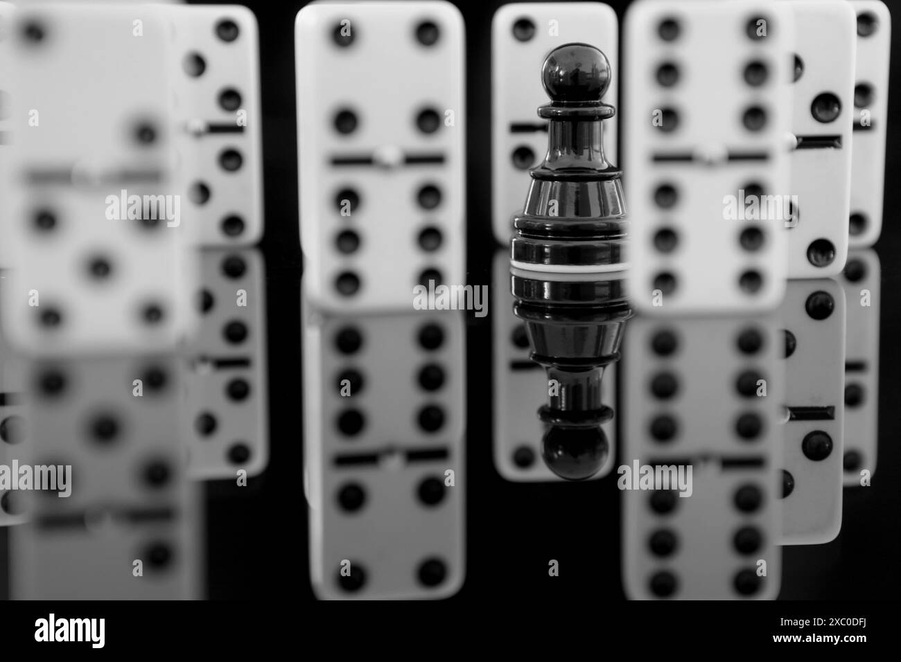 Primo piano di una pedina scacchiera nera tra pezzi di domino. Il concetto si distingue dalla massa Foto Stock