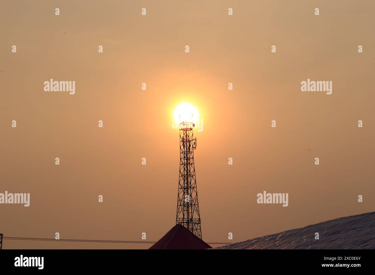 Una torre di telefoni cellulari solitaria si erge in alto sullo sfondo del sole che tramonta. Foto Stock