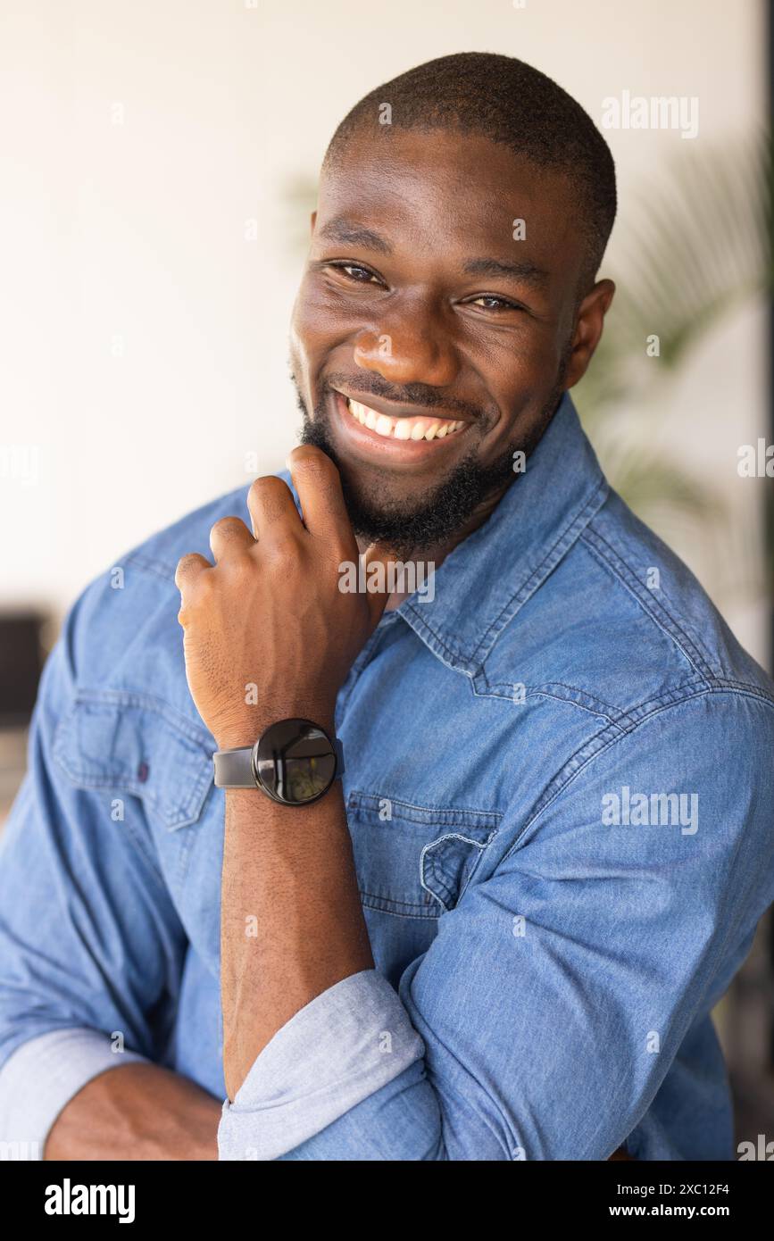 Uomo afroamericano sorridente, rilassato, con camicia in denim e orologio a casa Foto Stock