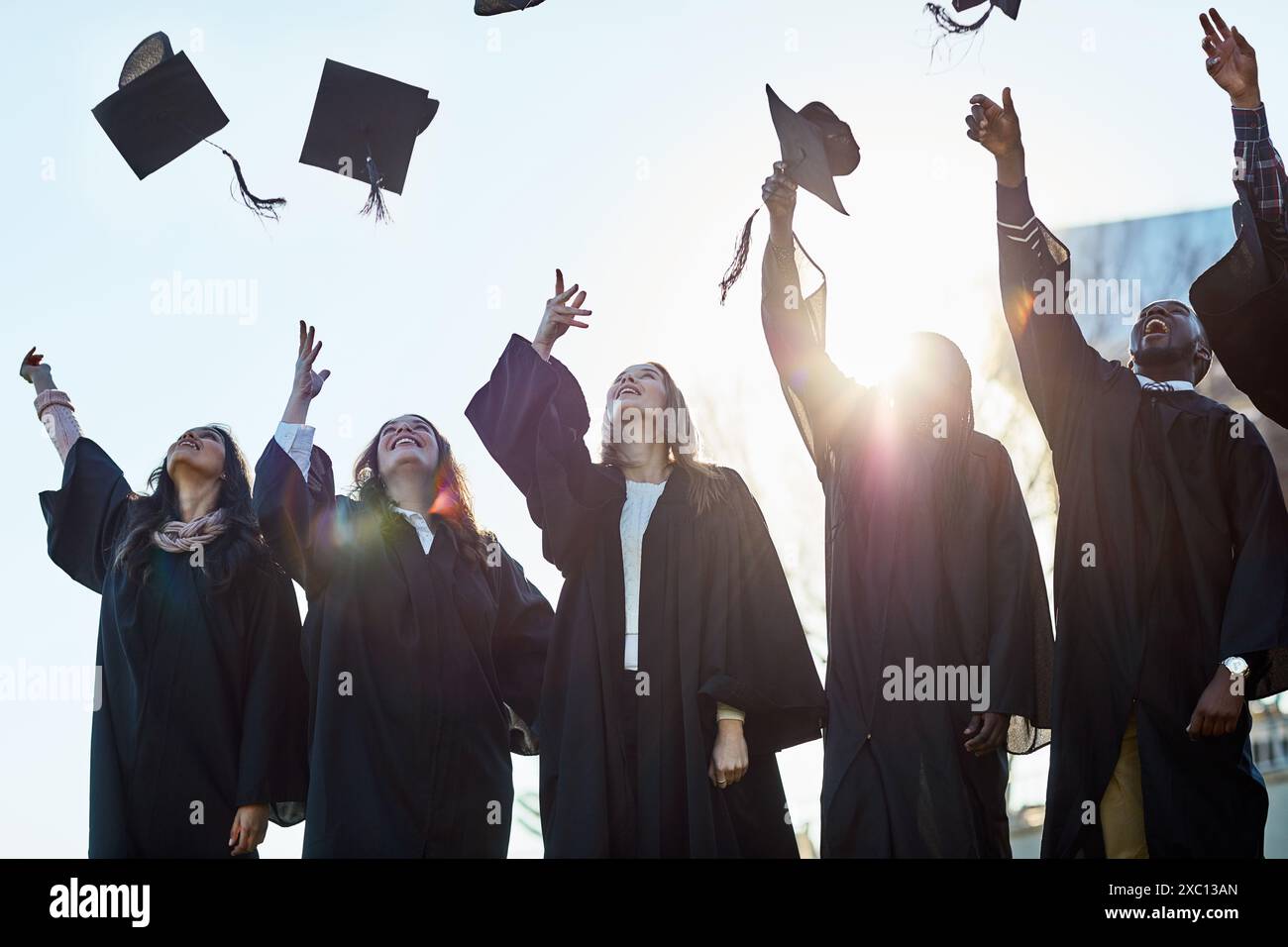 Gettate cappelli, college e studenti per la laurea, la cerimonia e il successo accademico all'aperto. Università, diversità e uomini e donne felici nel campus Foto Stock