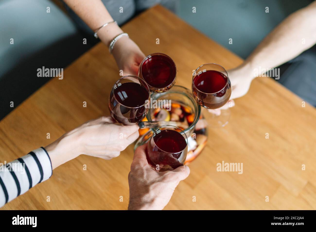 Un gruppo di persone brindano con bicchieri di vino rosso su un tavolo di legno con una caraffa di sangria Foto Stock