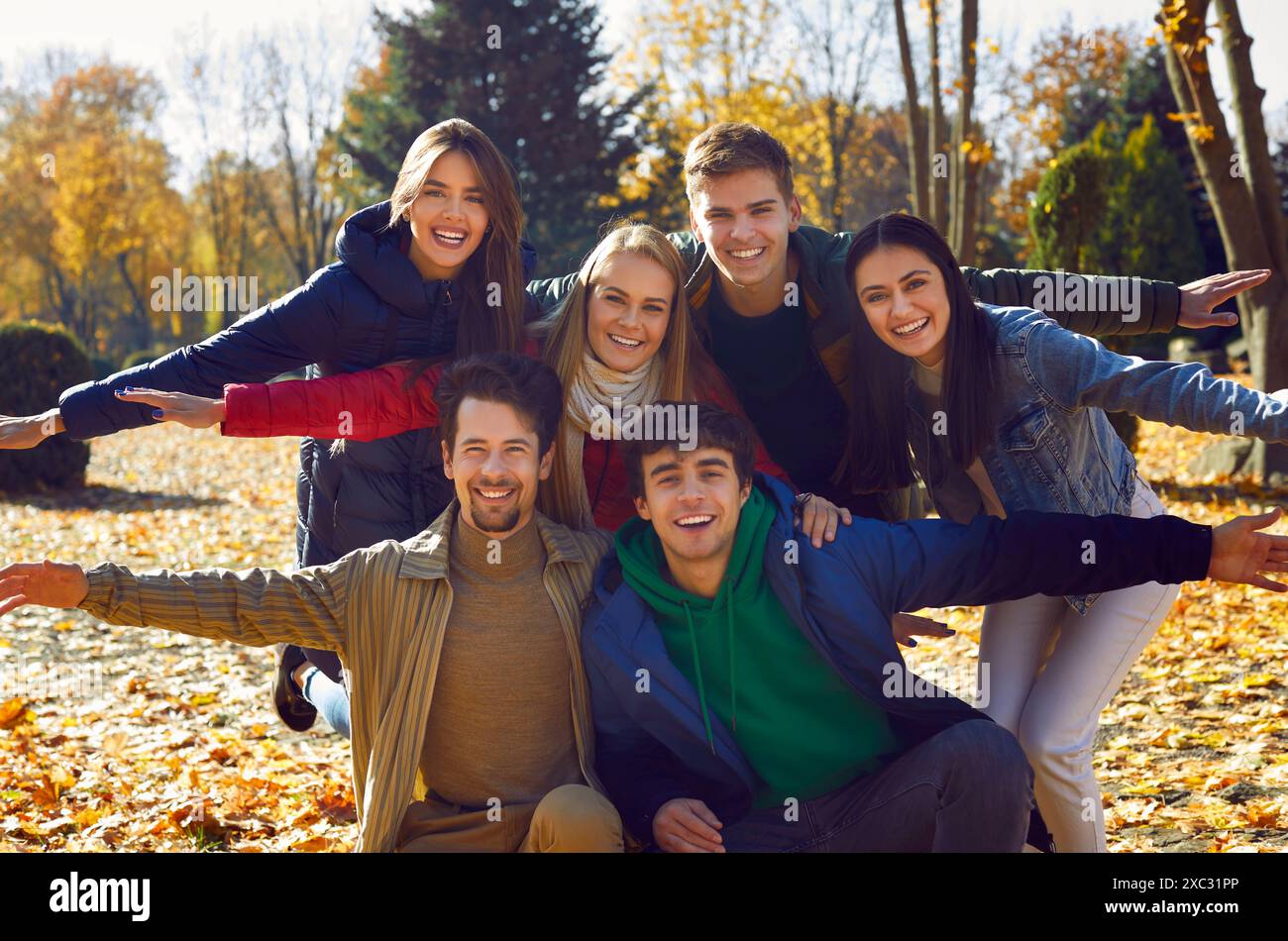Gli amici sorridenti in giacche e sciarpe posano per scattare foto, abbracciano e allargano le braccia ai lati. Foto Stock