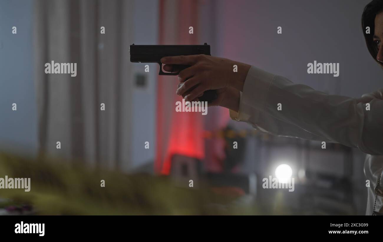 Donna ispanica che tiene la pistola in casa, forse raffigurante un crimine intenso o una scena thriller. Foto Stock