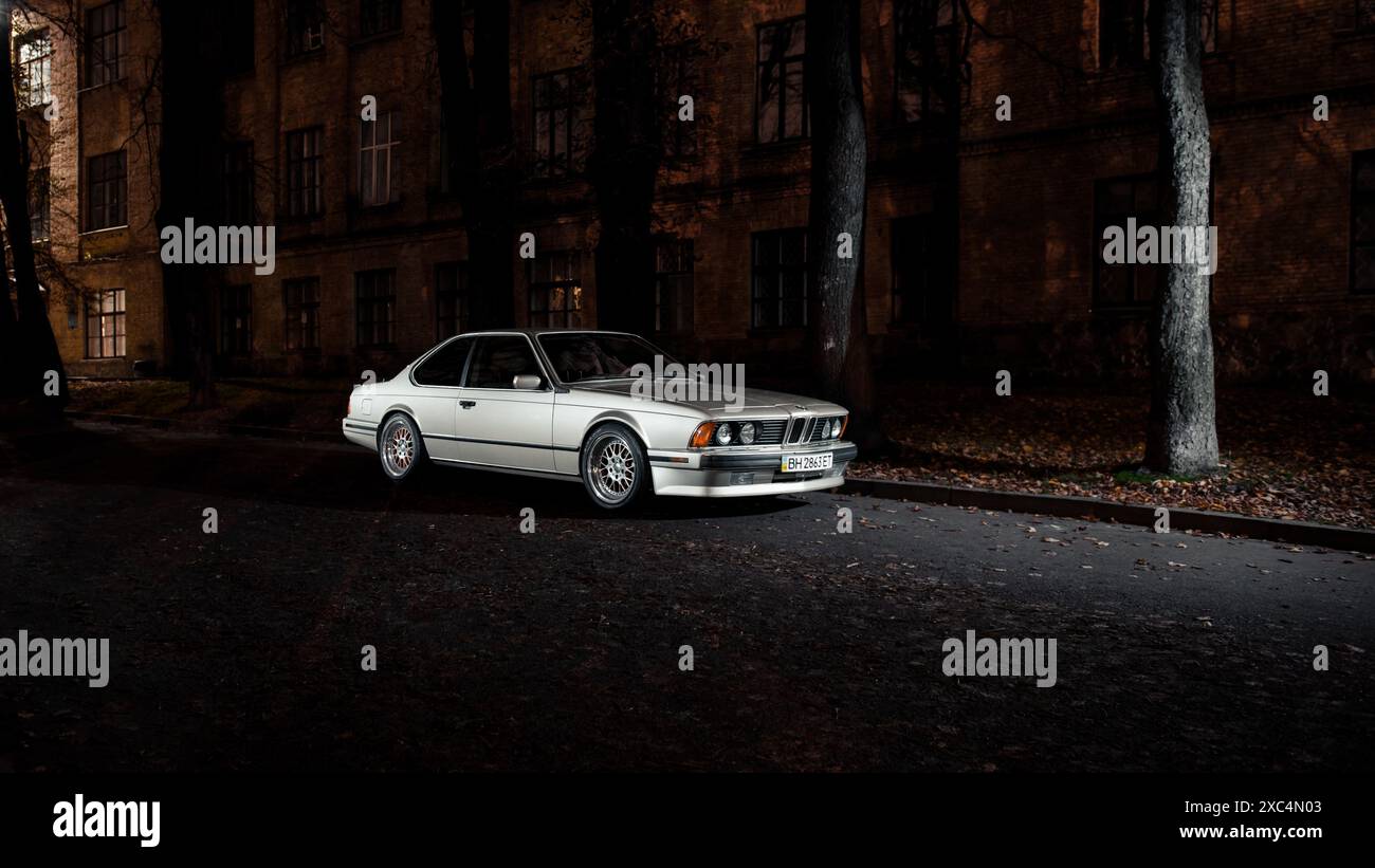 BMW 6 serie E24 coupé classica d'argento di notte nella città vecchia. Vista anteriore di tre quarti della BMW 1980-S "Sharknose" con fari rotondi. Foto Stock