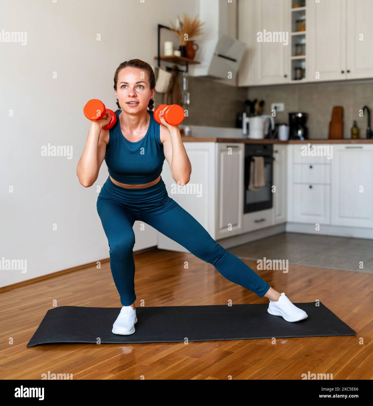 Donna sportiva che indossa abbigliamento sportivo per allenarsi con i manubri a casa. Stile di vita sportivo e sano. Foto Stock