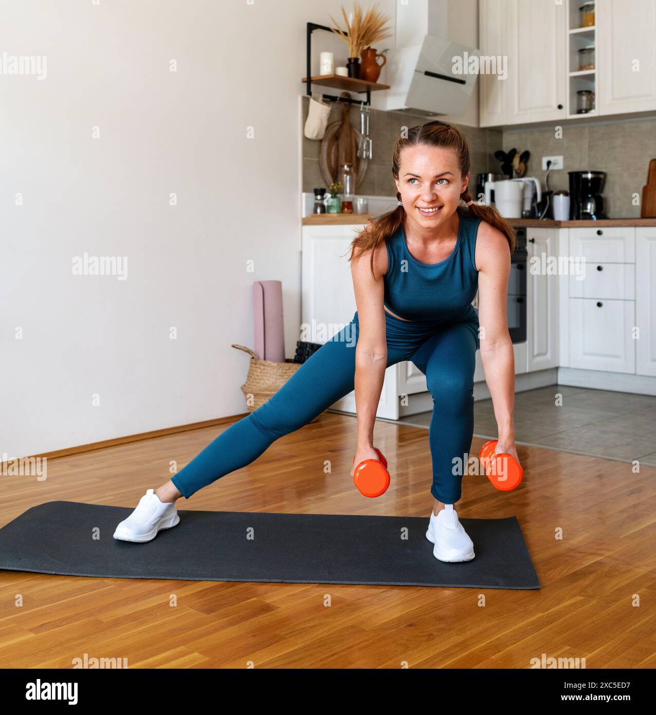 Donna motivata che indossa abbigliamento sportivo per allenarsi con i manubri a casa. Stile di vita sportivo e sano. Foto Stock