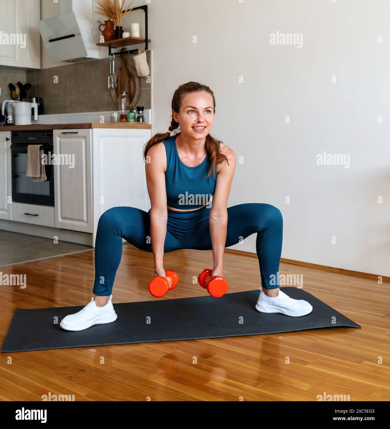 Donna atletica che indossa un abbigliamento sportivo per allenarsi con i manubri a casa. Stile di vita sportivo e sano. Foto Stock