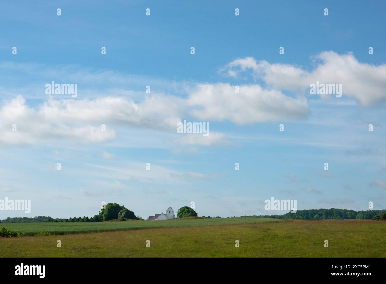 Vista sui campi di una chiesa bianca all'orizzonte di un paesaggio ondulato Foto Stock