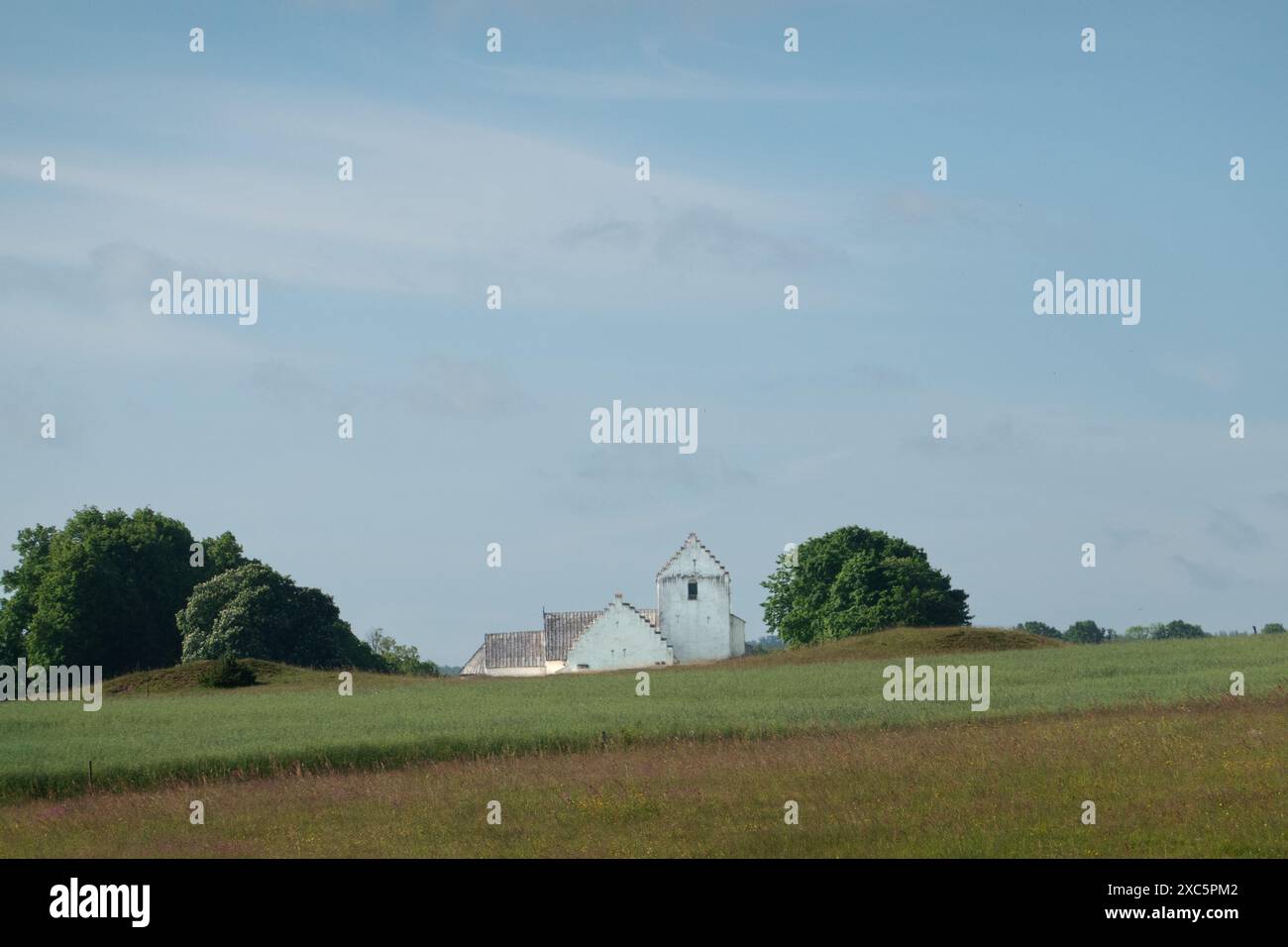 Vista sui campi di una chiesa bianca all'orizzonte di un paesaggio ondulato Foto Stock