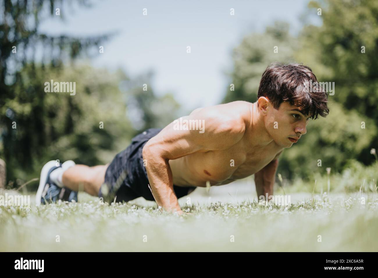 Giovane che fa push-up all'aperto nel parco soleggiato per fitness e allenamento di forza Foto Stock