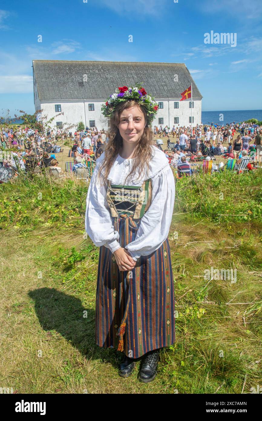 Giovane donna con una corona di fiori sulla testa e vestita con il costume folk di Smyge a una tradizionale festa di mezza estate con balli intorno a. Foto Stock