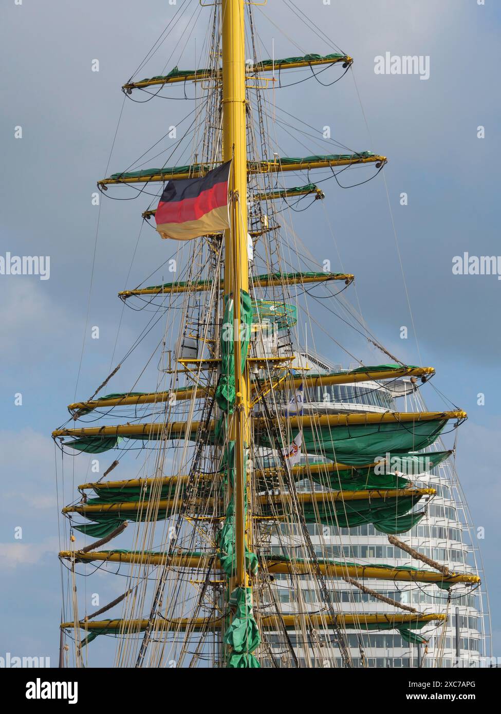 Vista dettagliata dell'albero di una nave a vela con bandiera e degli edifici moderni circostanti, bremerhaven, brema, germania Foto Stock