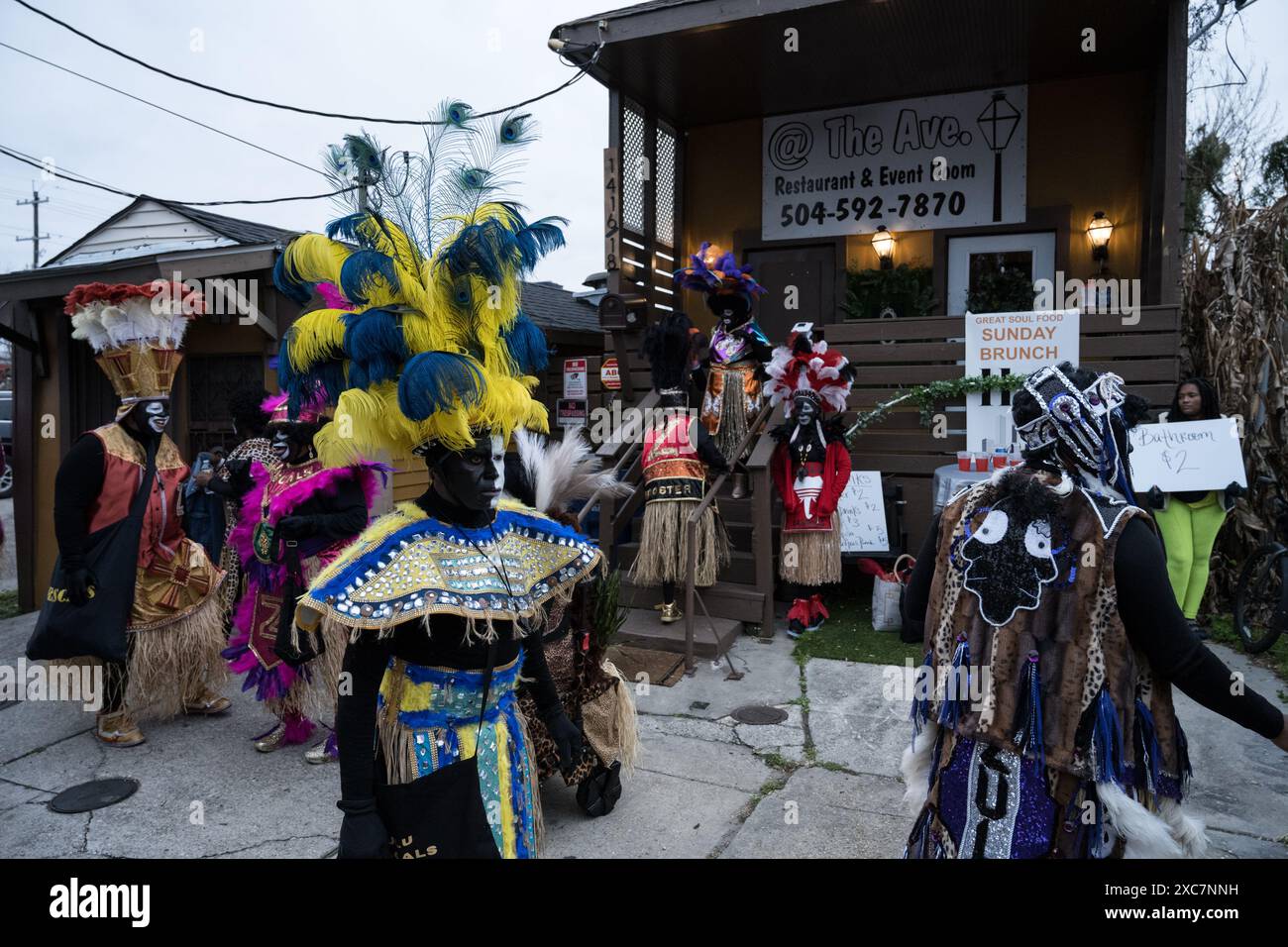 I membri Zulu krewe in elaborati costumi di piume e vernice per il viso si riuniscono fuori da un negozio, preparandosi per la parata annuale del Mardi Gras a New Orleans. Foto Stock