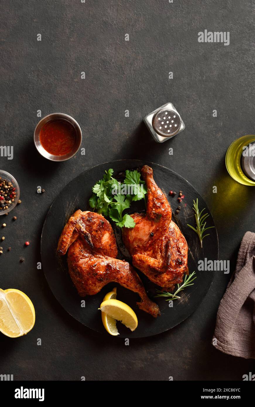 Metà pollo arrosto su un piatto di legno nero su sfondo di pietra scura con spazio libero. Carne di pollo alla griglia per cena. Vista dall'alto, disposizione piatta Foto Stock