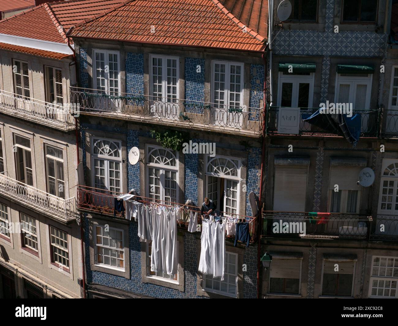 una vecchia donna sta appendendo il suo bucato appena lavato e i vestiti fuori dal suo balcone. Facciata colorata dell'edificio. Porto. Portogallo 29.05.2024 Foto Stock