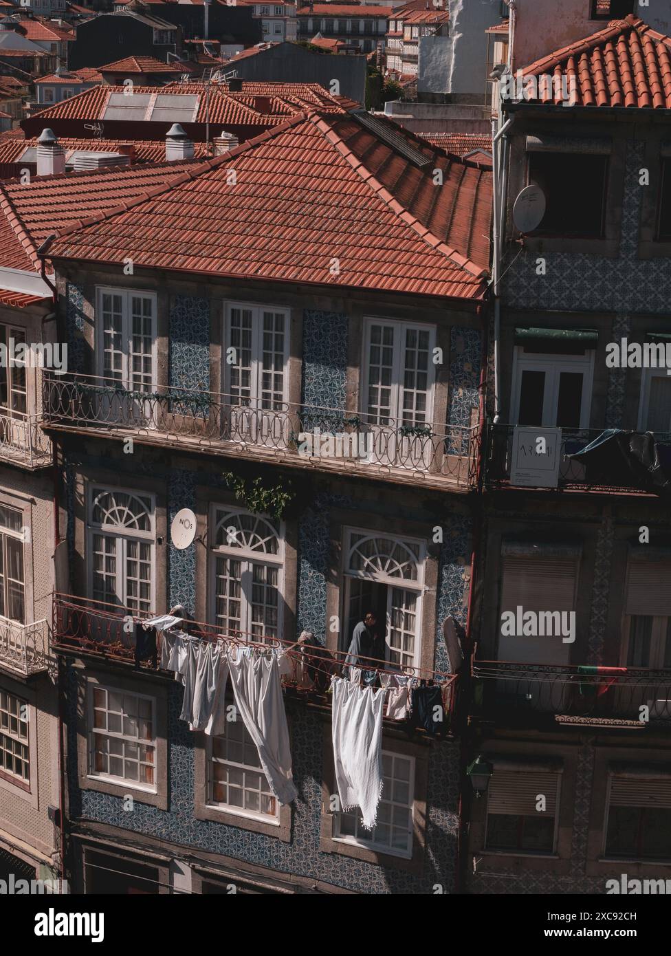 una vecchia donna sta appendendo il suo bucato appena lavato e i vestiti fuori dal suo balcone. Facciata colorata dell'edificio. Porto. Portogallo 29.05.2024 Foto Stock