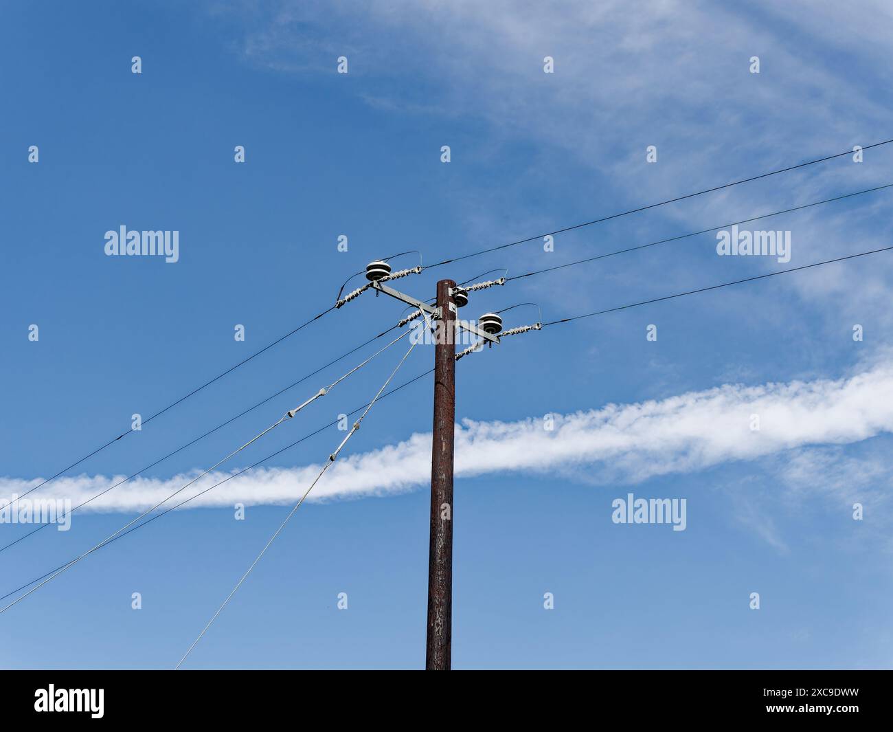 Un vecchio polo di alimentazione con linee contro un cielo blu con nuvole che simboleggiano una connettività duratura. Foto Stock