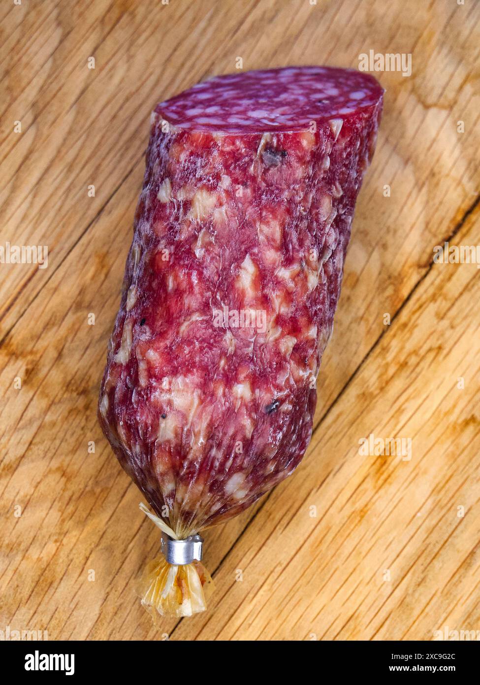Un pezzo di salame su una superficie in legno, che mostra il suo colore e la sua consistenza ricchi. Foto Stock
